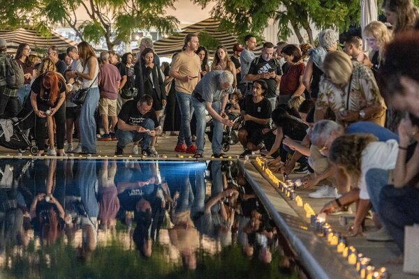 A crowd gathers around a pool, people’s reflections visible in the water. Candles burn around the perimeter, while people crouch down to light more.
