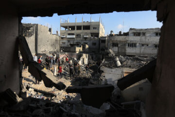 Several people stand in an open area amid bomb-damaged buildings.