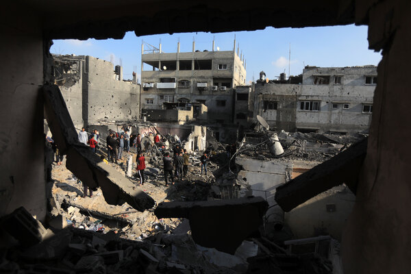 Several people stand in an open area amid bomb-damaged buildings.